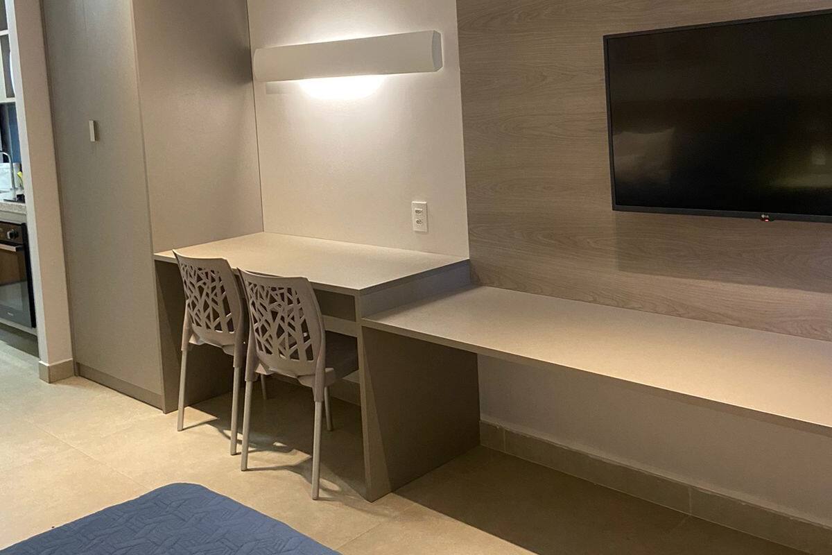 A modern living room with a built-in TV, a dining table with chairs, and a blue rug.