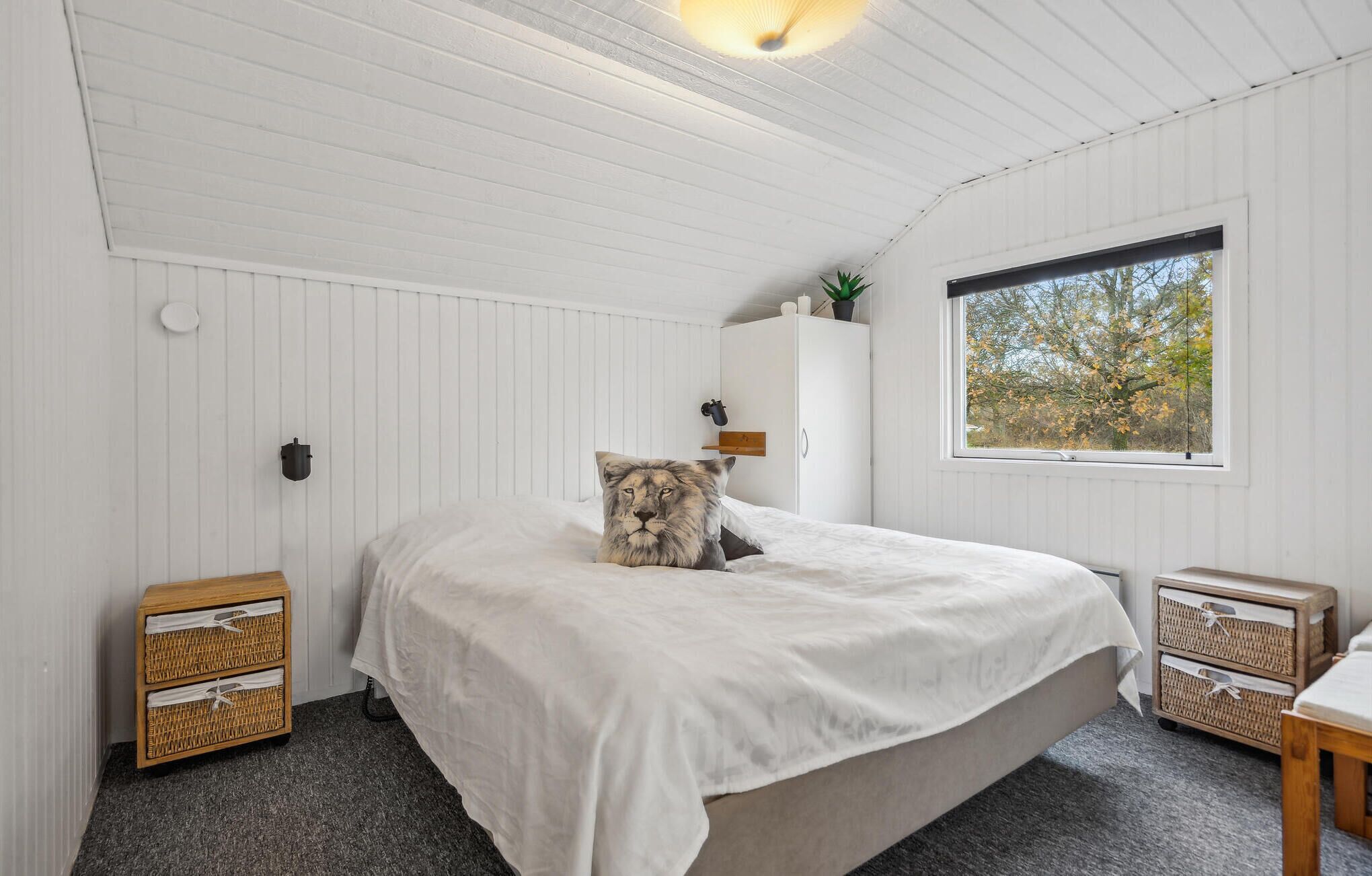 Un dormitorio con una cama grande, paredes blancas, un ventanal y dos cestos de mimbre.