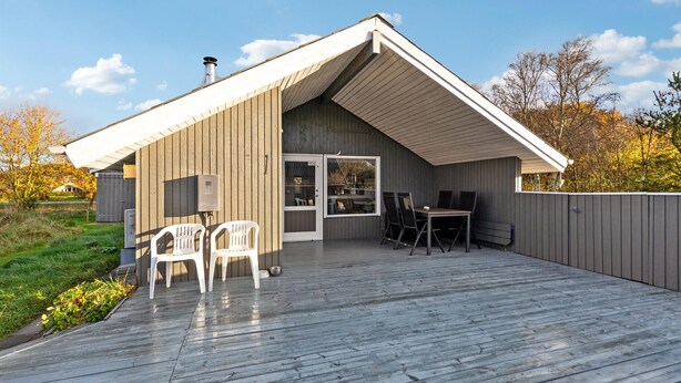 A modern house with a wooden deck, a dining area with a table and chairs, and a large sliding glass door.