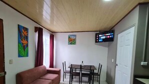 Un salon comprenant un canapé, une table à manger avec des chaises, un téléviseur fixé au mur et une porte.
