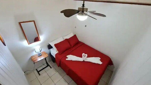 Une chambre d’hôtel avec un lit, un ventilateur de plafond, une table de chevet avec une lampe et un miroir au mur.