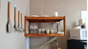 Une cuisine avec une étagère en bois où sont rangés divers ustensiles et articles en verre.