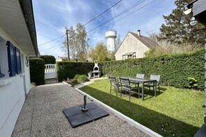 Um pátio com mesa e cadeiras, churrasqueira, torre d'água e um sebedo.