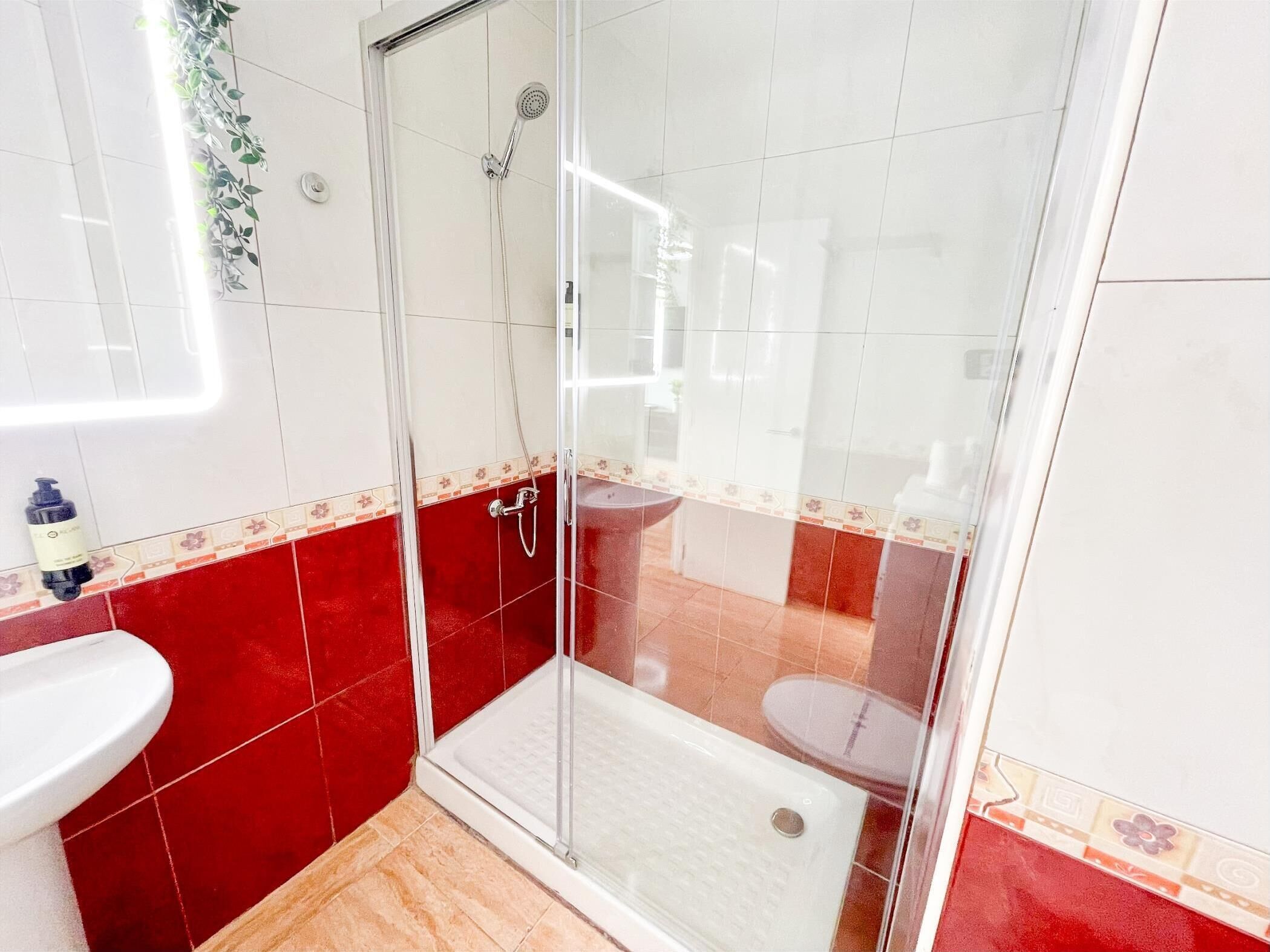 Une salle de bain avec une douche à parois de verre, un lavabo blanc et des murs recouverts de carreaux rouges.