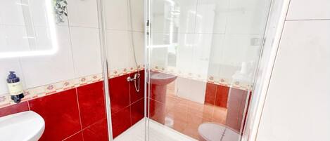 Une salle de bain avec une douche à parois de verre, un lavabo blanc et des murs recouverts de carreaux rouges.