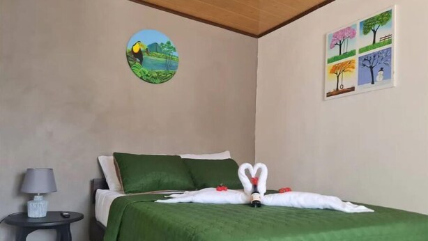 A hotel room with a bed, green bedding, a wall art of a landscape, and a small table with a lamp.