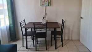 A dining area with a table and four chairs, a painting on the wall, and a door to the right.
