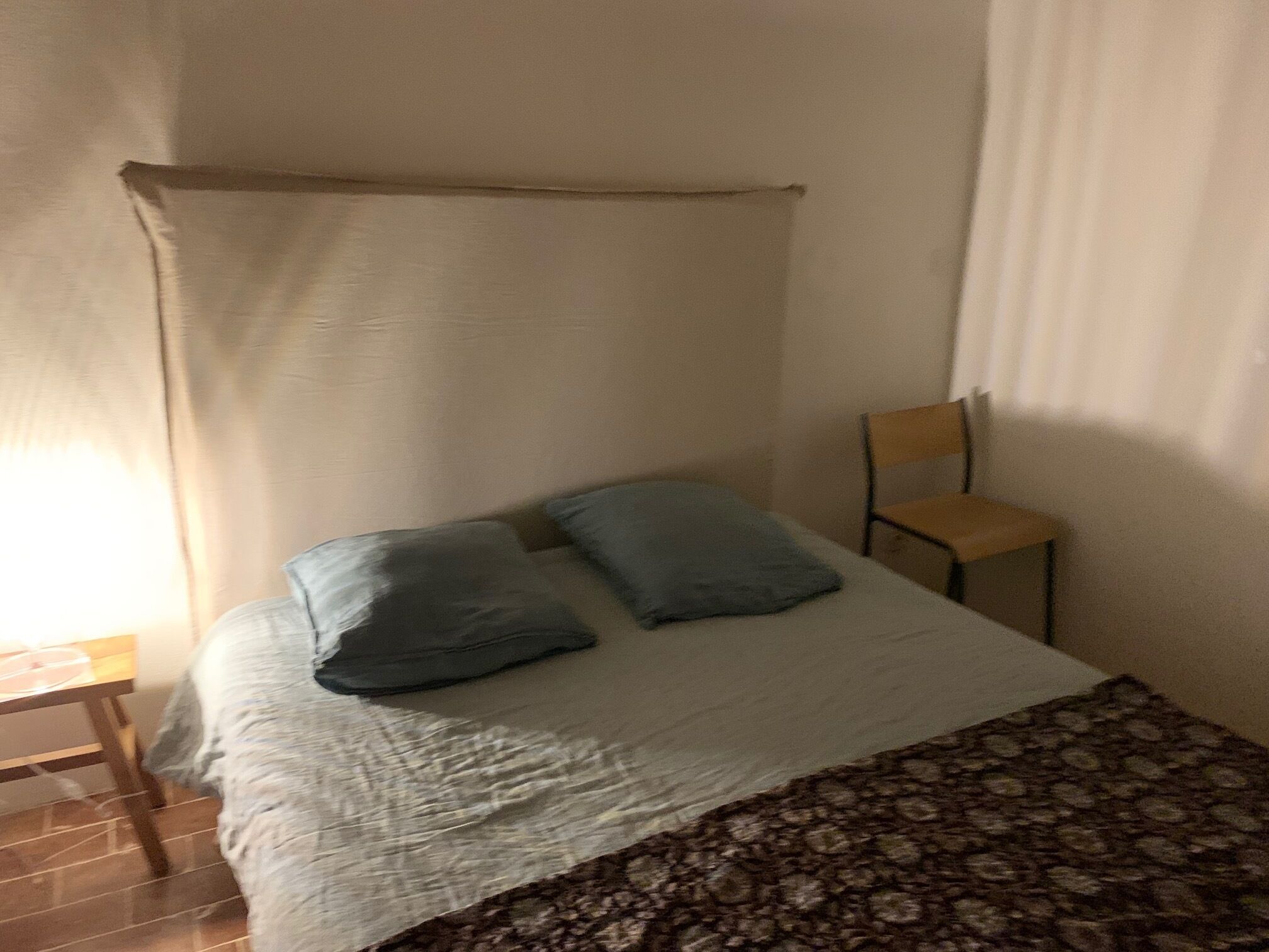Een eenpersoonsbed met hemelbed, twee kussens, een stoel en een bedsprei met dessin.