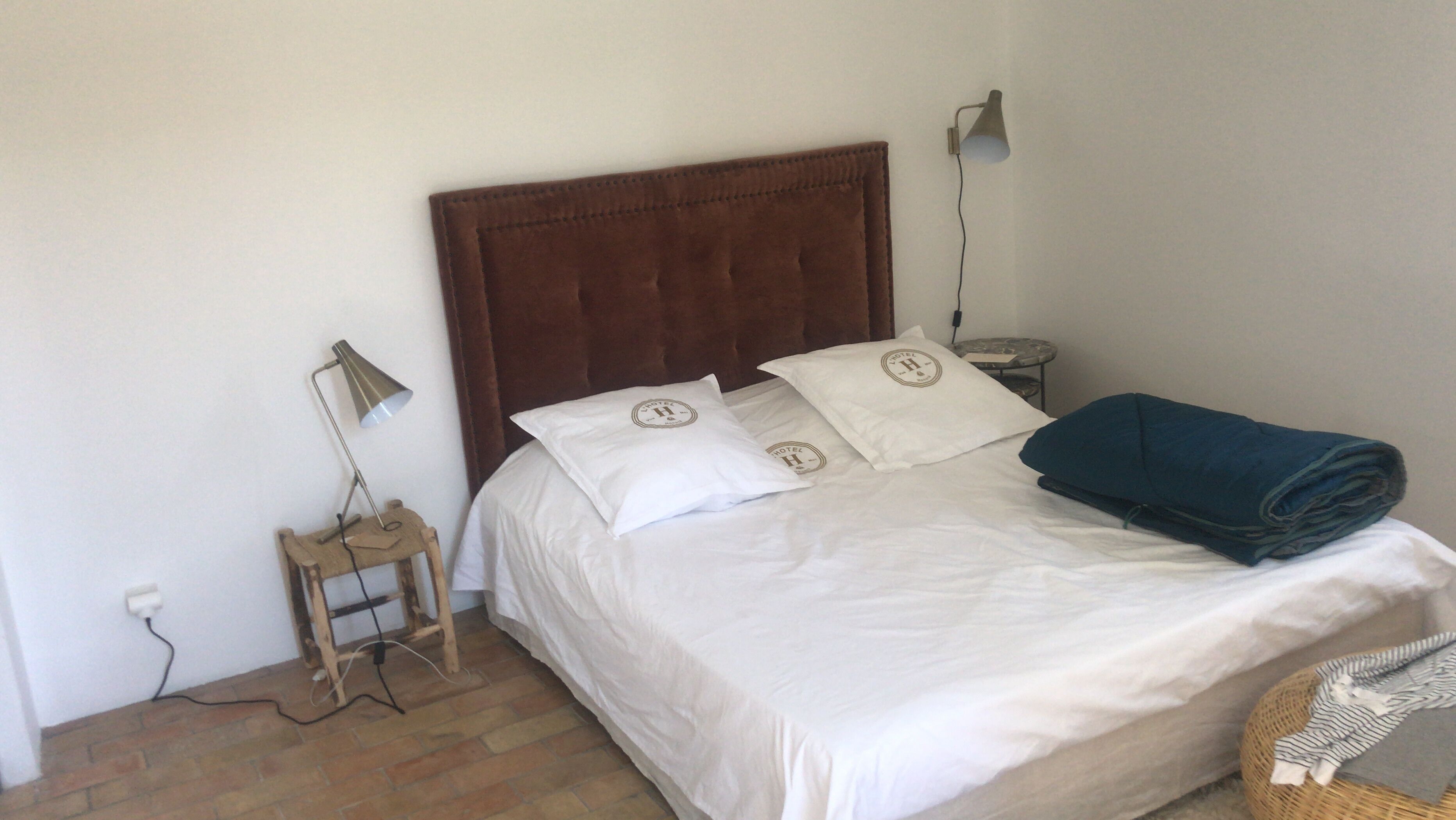 A neatly made bed with white linens and pillows, a wooden nightstand with a lamp, and a rolled towel on the bed.