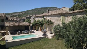 A stone building with a swimming pool, outdoor seating, and a view of a hill. - Large country house in a village in the Lubéron park, Forcalquier country (Limans)