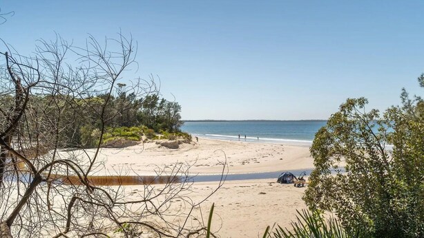 A beach with a tent set up, surrounded by sparse vegetation and a clear sky.
