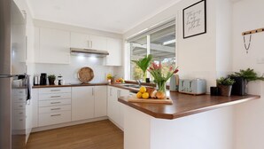 A modern kitchen with white cabinetry, a wooden countertop, a stainless steel range hood, a toaster, and a window with a view of greenery.