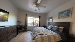 A bedroom with a bed, a desk, a chair, a ceiling fan, and a view of the outdoors.