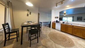 A spacious dining area with a large table and chairs, a kitchen with wooden cabinets, and a tiled floor.