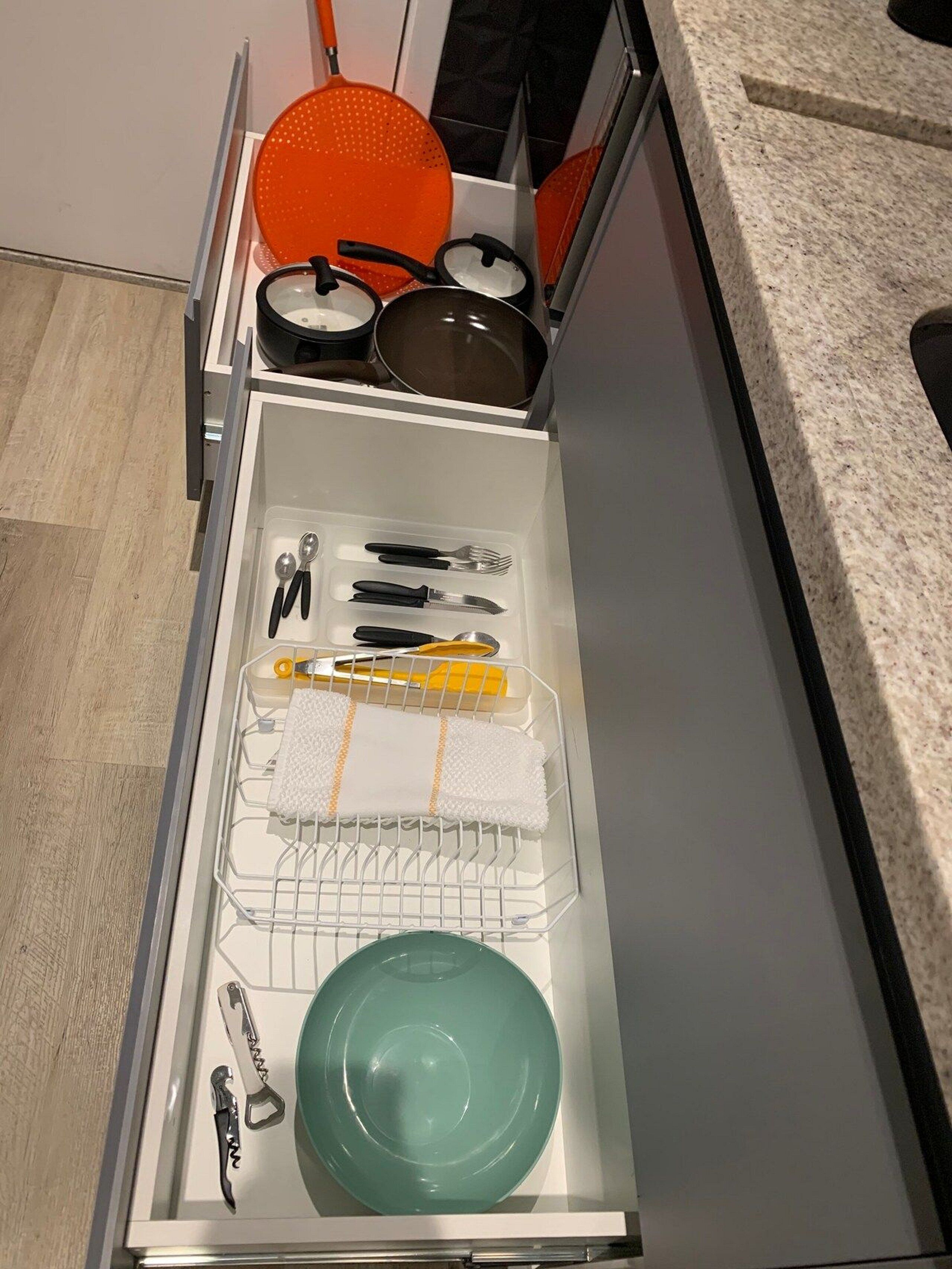 A kitchen drawer with utensils, a cutting board, a dish rack, and a plate.
