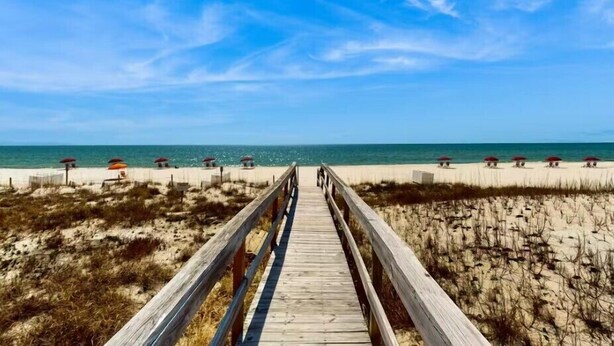 Una pasarela de madera que conduce a una playa con sombrillas y un cielo despejado.