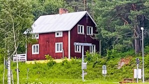 Ein rotes Holzhaus mit Metall-Dach, umgeben von üppigem Grün und Bäumen.