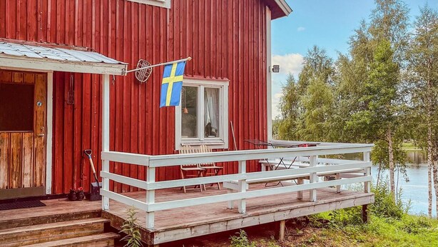 Ein rotes Holzhaus mit weißem Veranda und einer schwedischen Flagge.