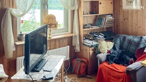 Ein gemütliches Zimmer mit einem Holztisch, einem Computer, einem Bücherregal und einem Hund, der auf einem Stuhl ruht.