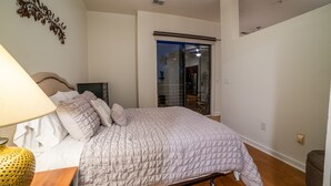 Une chambre à coucher comprenant un lit, une table de chevet, une lampe, un élément décoratif mural et une porte-fenêtre coulissante donnant sur l’extérieur.