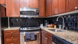 Une cuisine avec des meubles en bois, une cuisinière en acier inoxydable, un four à micro-ondes, un lave-vaisselle et un dosseret de carrelage noir.