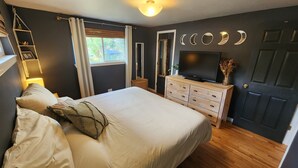 Une chambre à coucher comprenant un lit, une commode, un téléviseur et une porte décorée de motifs représentant les phases de la lune.