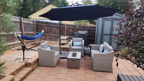 Une terrasse extérieure aménagée avec des meubles en osier, un hamac et un barbecue.