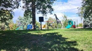 Une aire de jeux avec des toboggans et des balançoires, entourée d’arbres et d’une pelouse.