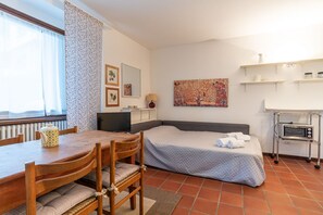 Une chambre comprenant un lit, un bureau avec un ordinateur, une télévision, un tableau et un coin cuisine.