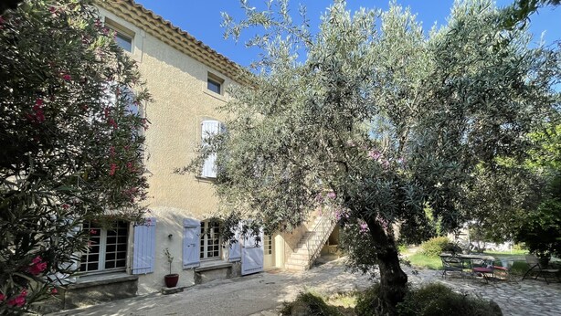 A courtyard with a stone-paved area, a building with a tiled roof, and a tree with pink flowers.