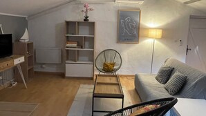 A cozy living room with a sofa, a chair, a small table, a bookshelf, and a TV.