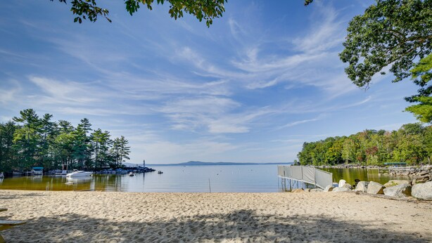 Une plage avec un rivage sablonneux, un lac paisible et une jetée en bois qui s’avance dans l’eau.