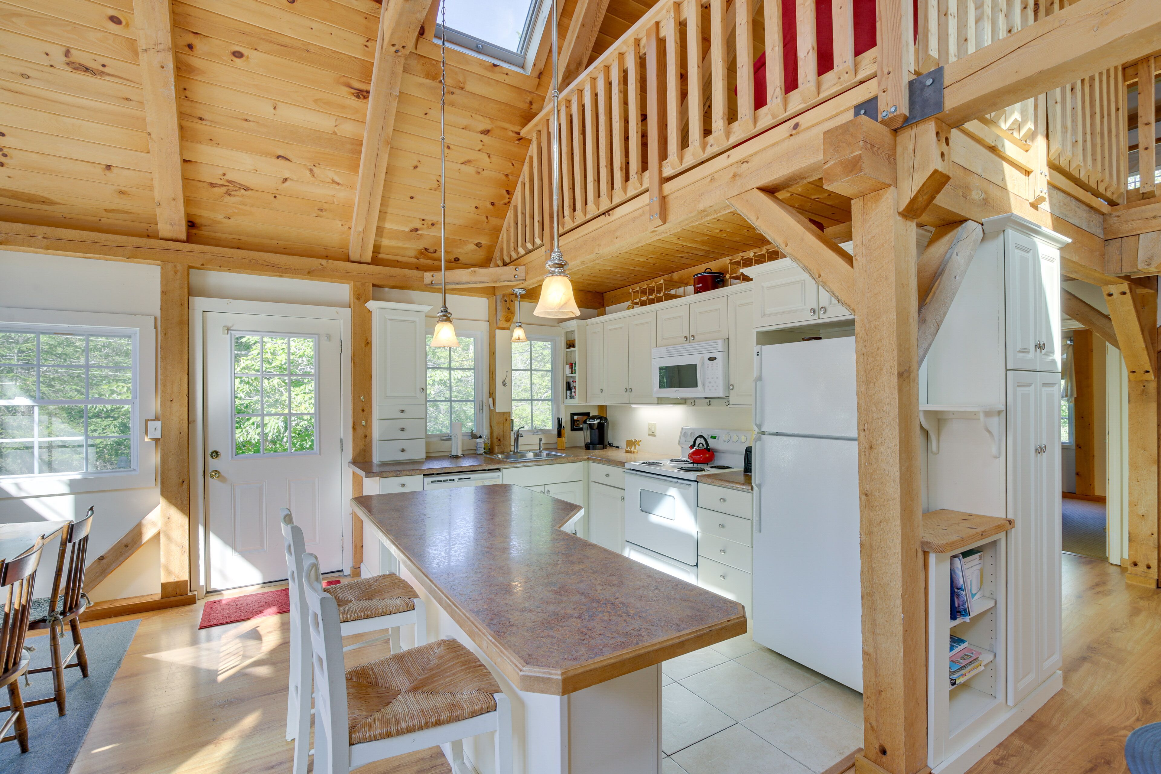 Une cuisine spacieuse avec un grand îlot central, des poutres en bois et un espace en mezzanine.