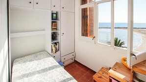 Un dormitorio con cama, armario, escritorio con silla y ventana con vista a la playa.