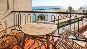 Una mesa de madera y sillas de mimbre en un balcón con vista a una playa y al océano.