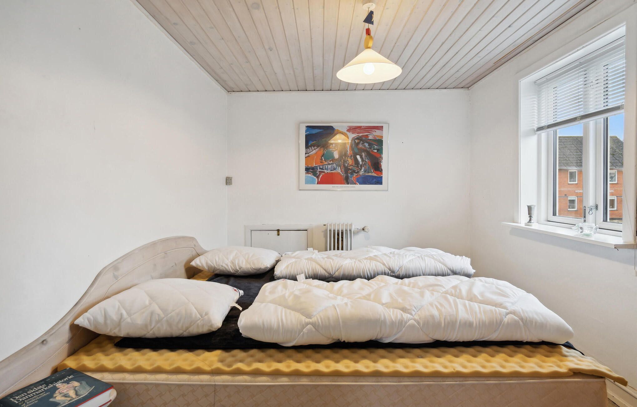 A bedroom with a bed, a radiator, a window with blinds, and a ceiling light.