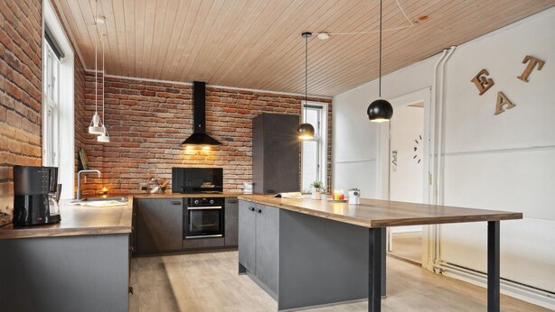 A modern kitchen with a brick wall, wooden ceiling, and a central island.