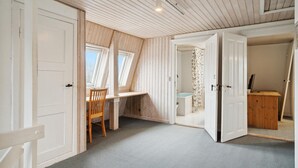 A room with a sloped ceiling, skylights, a wooden desk, a chair, and a bathroom with a shower and toilet.