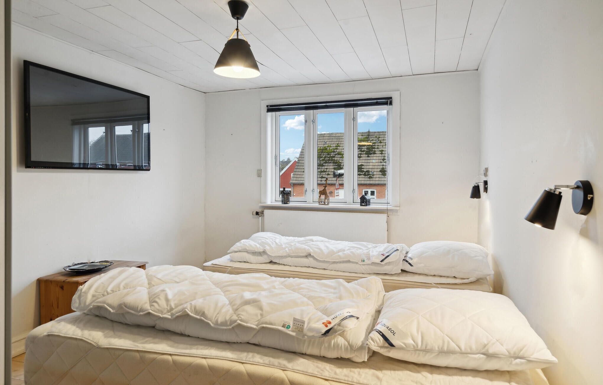A bedroom with two beds, a window with a view of buildings, a ceiling light, and a wall-mounted lamp.