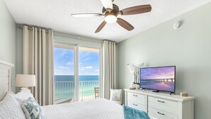 Une chambre avec un lit, une télévision, un ventilateur de plafond, une table de chevet et une vue sur l’océan.