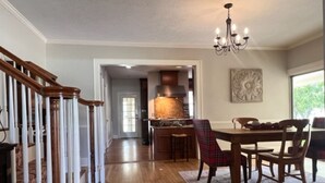 Un comedor amplio con una mesa y sillas de madera, un candelabro y vistas a la cocina al fondo.