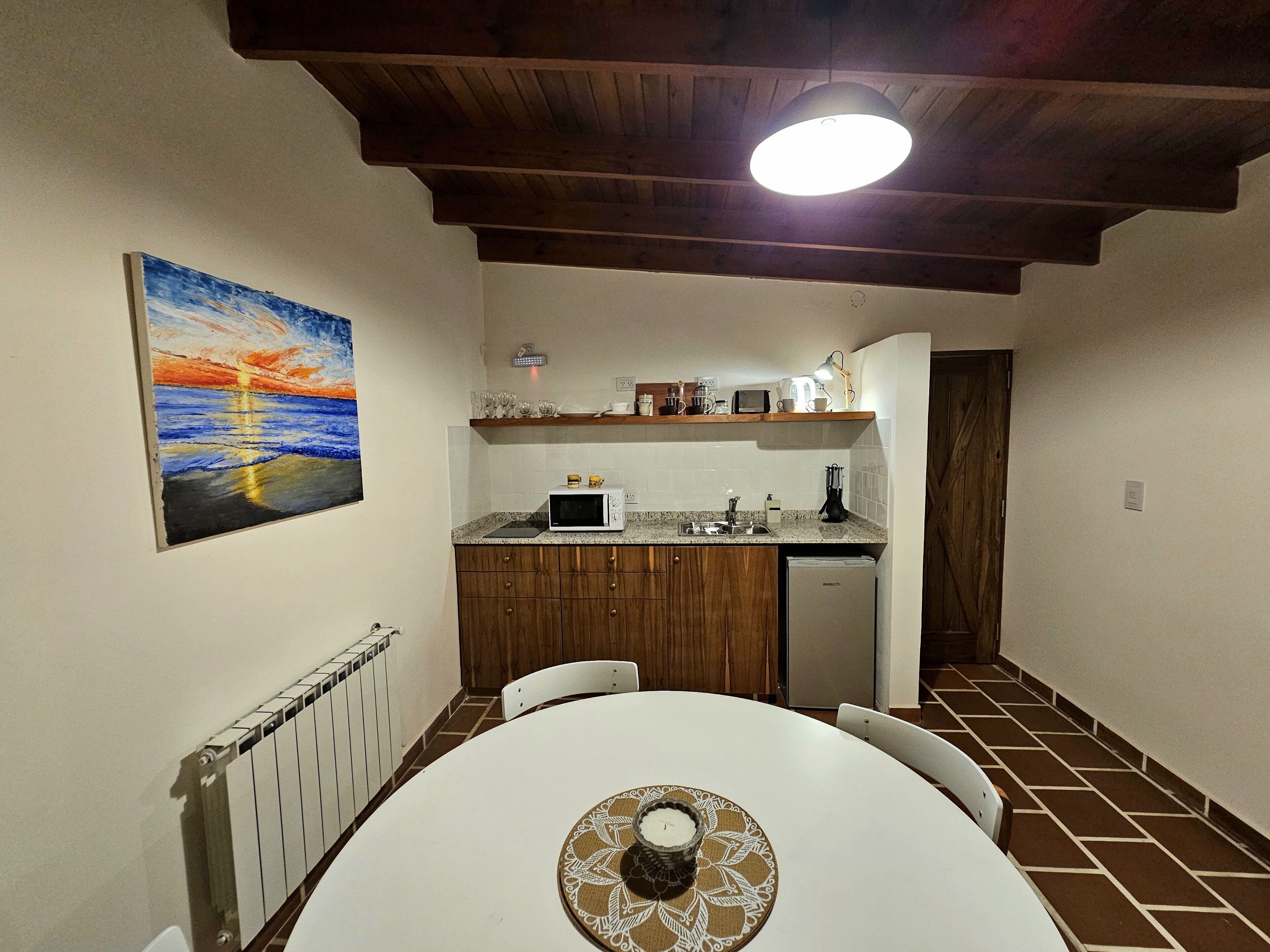 A compact kitchen with a white countertop, wooden cabinets, and a dining table with a decorative coaster.