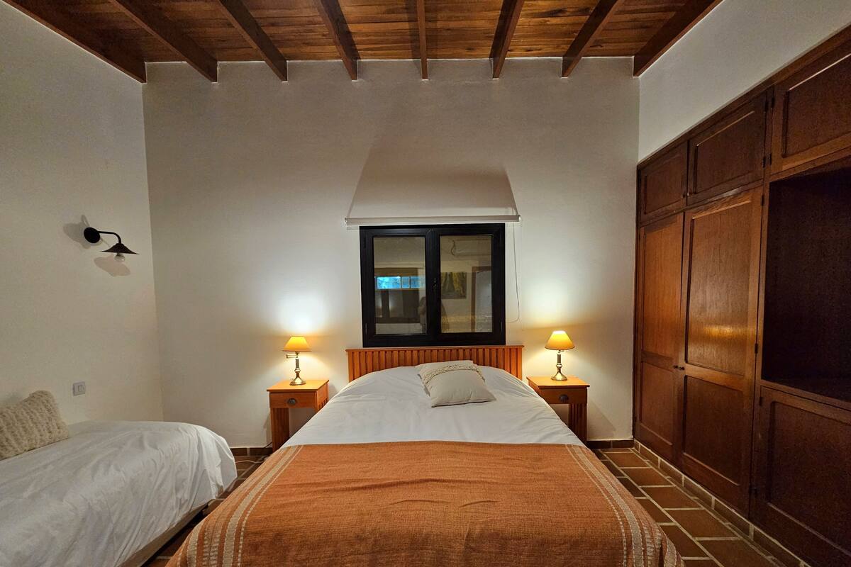 Une chambre à coucher avec un grand lit, deux tables de chevet avec des lampes, une armoire en bois et une fenêtre donnant sur un beau paysage.