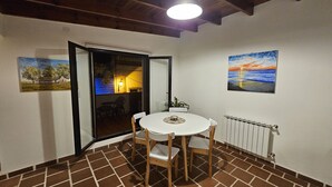 A dining area with a round table and chairs, a view through an open door to an outdoor patio, and two paintings on the walls. - Posada del Atelier (San Antonio de Areco)