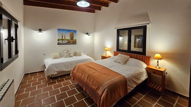 A bedroom with two beds, a large window, and a wooden ceiling. - Posada del Atelier (San Antonio de Areco)