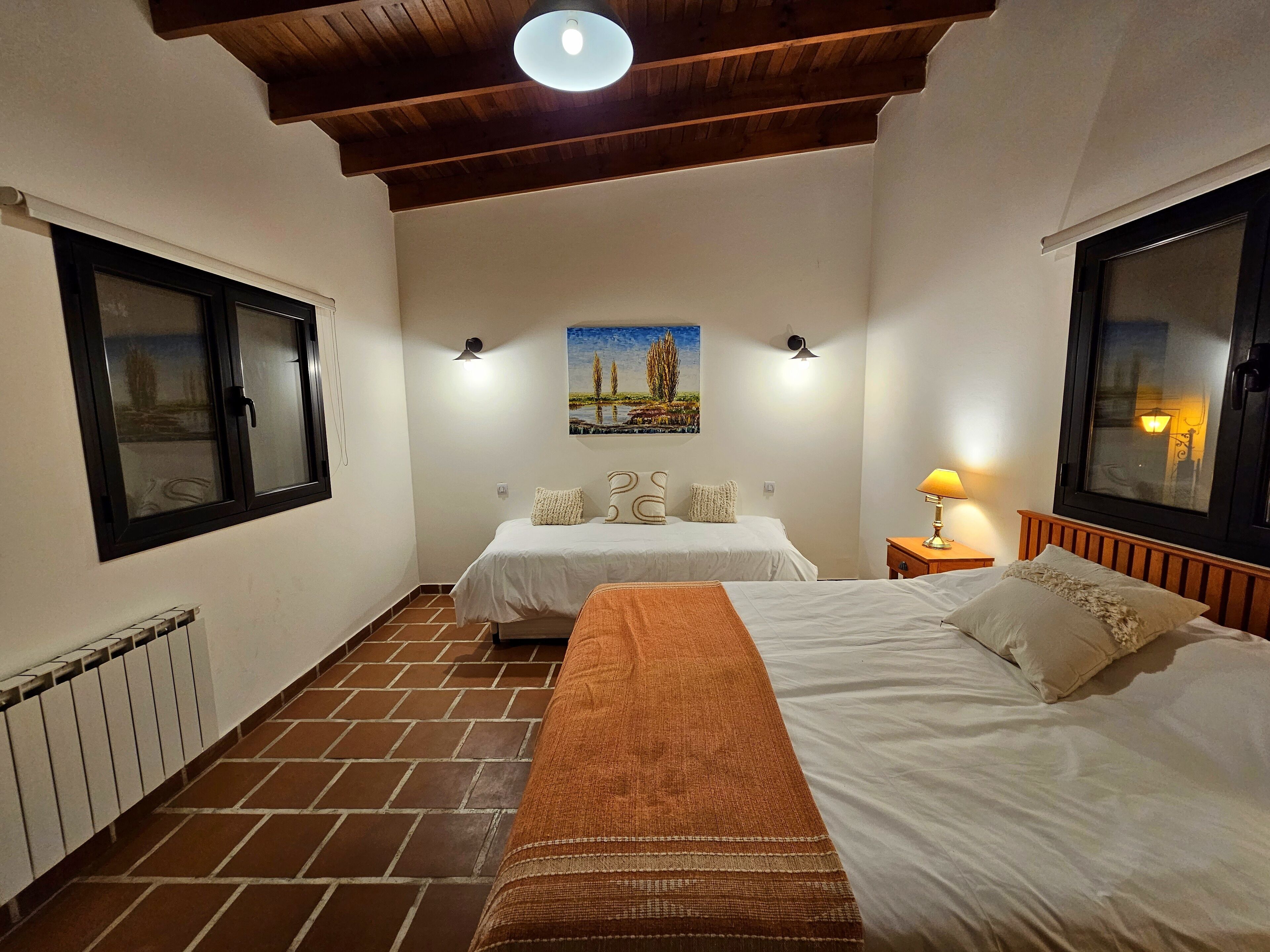 Une chambre d’hôtel avec deux lits, un radiateur, un tableau au mur et une fenêtre donnant sur un beau paysage.