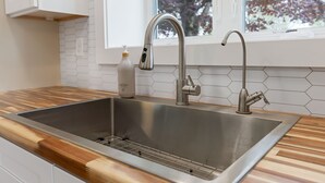 Una cocina moderna con un lavamanos de acero inoxidable, encimera de madera y ventana con vista a árboles.
