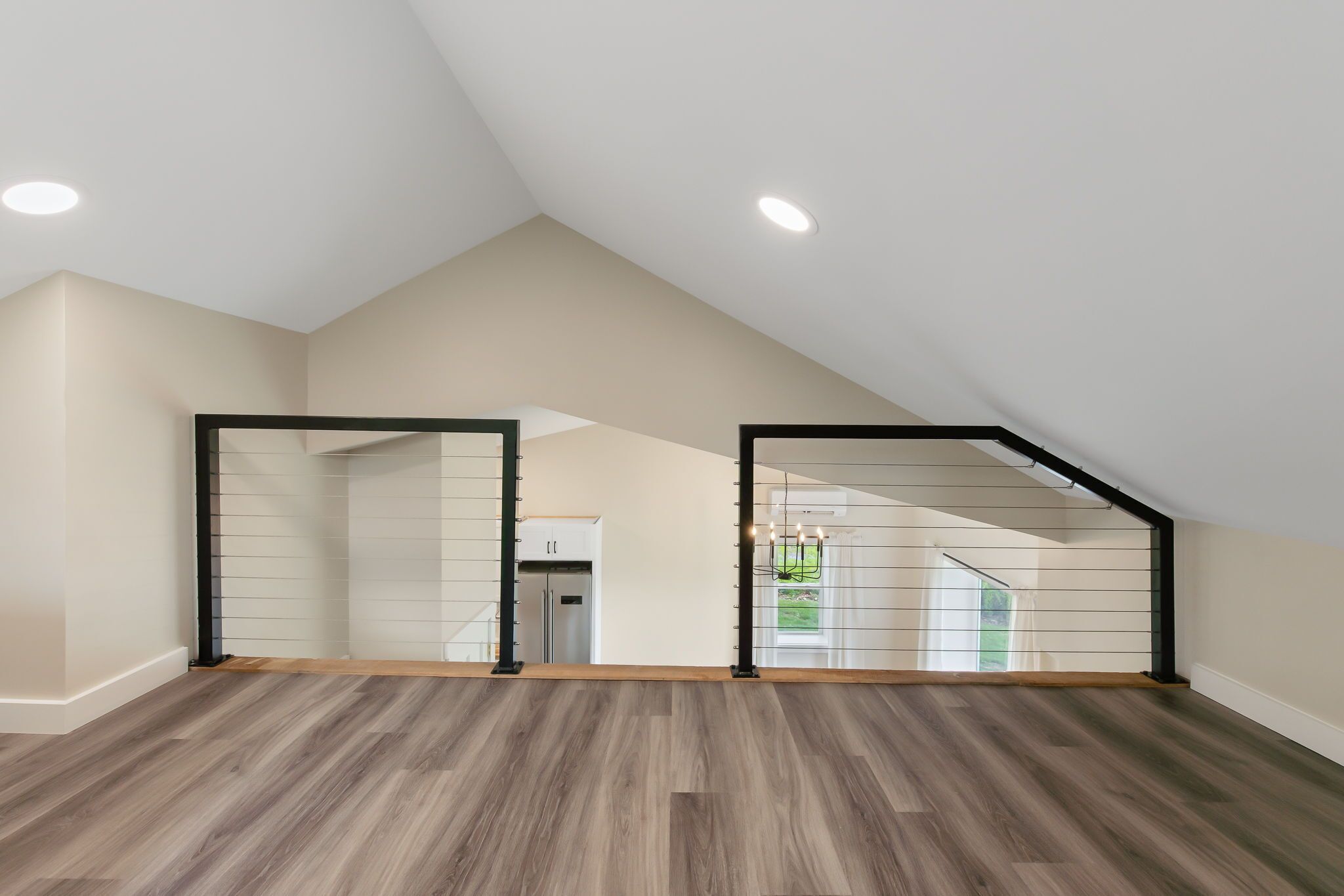 Un'ampia stanza mansardata con soffitto spiovente, pavimento in legno e vista su una cucina e uno spazio esterno attraverso una porta vetrata.