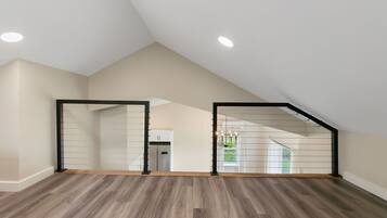 Un'ampia stanza mansardata con soffitto spiovente, pavimento in legno e vista su una cucina e uno spazio esterno attraverso una porta vetrata.