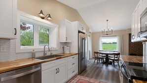 Una cocina moderna con armarios blancos, un refrigerador de acero inoxidable y una zona de comedor con mesa y sillas.